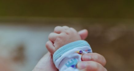 An adult hand holds a baby hand. Connection with your baby from early pregnancy is important.
